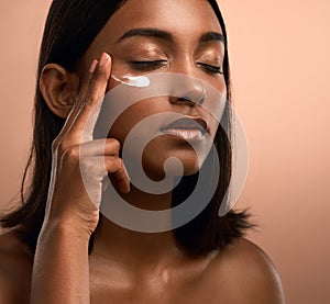 All the vowels vow to hold my name. an attractive young woman applying moisturiser against a brown background.