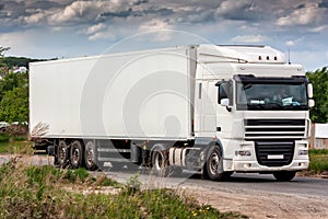 All white long-distance truck with a semitrailer moves in the countryside