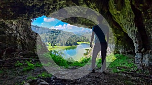 Allakogel - Hiking man walking out of dark cave Drachenhoehle with scenic view of alpine lake Sackwiesensee