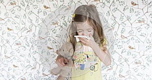 An allergic child sneezes into a handkerchief. Symptoms of influenza and the common cold in primary school children. Girl with a