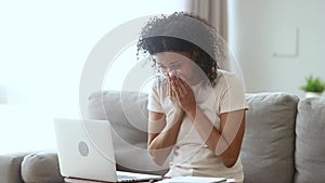 Allergic ill african woman blowing nose sneezing working from home
