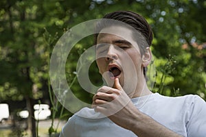 Allergic young man sneezing in park