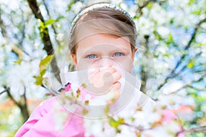 Allergy. Little girl is blowing her nose near spring tree in bloom - sneezing girl