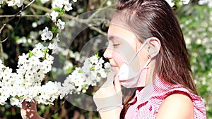 Allergy season. A young girl in a medical mask sniffs Apple blossoms