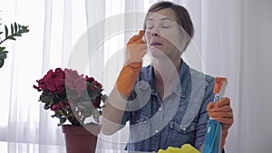 Allergy season, young woman in gloves uses spray detergent and sneeze from cleaning