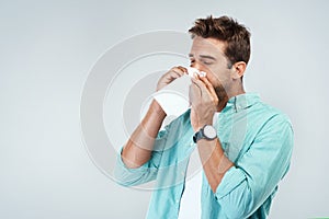 Allergy, sick and man blowing nose in tissue with flu, illness and virus on studio background. Health mockup, wellness