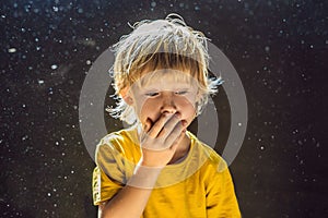 Allergy to dust. Boy sneezes because he is allergic to dust. Dust flies in the air backlit by light