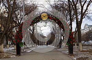 Alley with lanterns and benches under an iron arch decorated with red roses with a clock. Spring city beautiful landscape