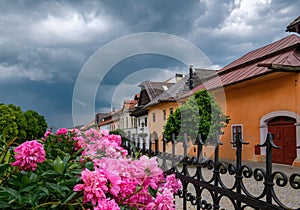 Ulička so starými historickými budovami a letná záhrada s kvetmi a búrkovými mrakmi. Spišská Sobota, Poprad, Slovakia.