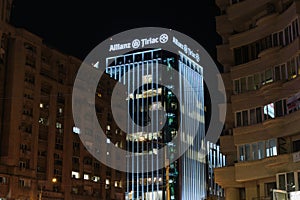 Allianz-Tiriac Tower illuminated office building between regular buildings at Victory Square at night