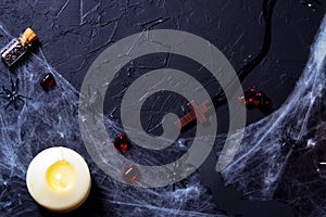 alloween wooden cross lying next to a burning candle on a web with spiders and bats on a black background. horizontal, flat lay,