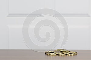 Pile of gold coloured coins on a table surface with soft focus white panel behind