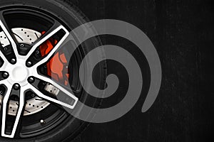 Alloy wheels of racing car with metal brake discs and red caliper on a black cement wall background with copy space your writing