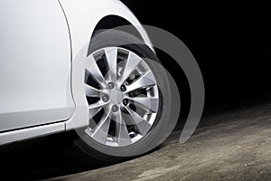 Alloy wheels of a white car are turning on the cement road