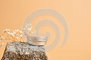 alluminum cream jar on stone with dry flowers on beige background