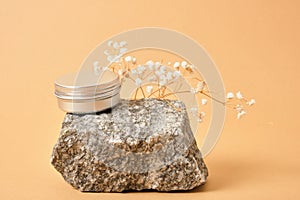 alluminum cream jar on stone with dry flowers on beige background