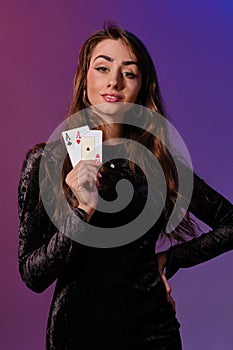 Brunette woman in black velvet dress showing two playing cards, posing against coloful background. Gambling