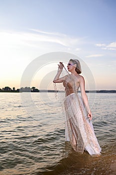 Alluring Sensual Sea Mermaid Blond Woman With Artistic Makeup and Strasses on Face Posing on Ocean Waves with Silver Crown And Net