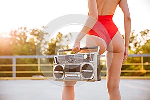 Alluring woman in swimsuit standing outdoors and holding old boombox