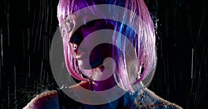 Alluring young woman with pink wig is standing under water flows in darkness, closeup portrait