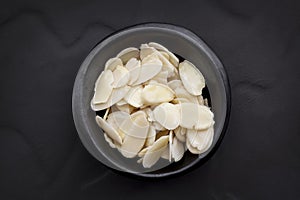 Almond Flakes in Black Bowl over Dark Slate Overhead View.