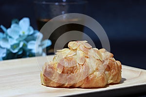 Almond flavor croissant placed on the square wooden tray with out focus tea in a glass and blue flowers on dark background