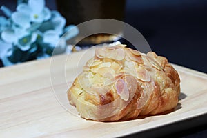 Almond flavor croissant placed on the square wooden tray with out focus tea in a glass and blue flowers on dark background