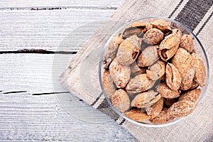 almond on glass plate on light grey linen napkin on white wooden background, top view on right side