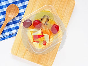 Almond jelly Tao Huay Fruit Salad topping mix fruit on chopping board and spoon, blue checkered napkin over white background.