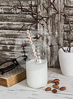 Almond milk and almonds, a book, glasses on rustic light wood table.