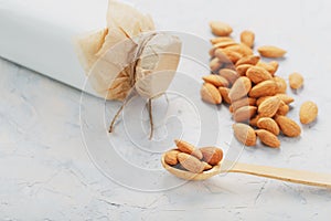 Almond milk in a bottle with a handful of seeds and a wooden spoon on a light background.