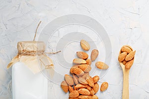 Almond milk in a bottle with a handful of seeds and a wooden spoon on a light background.