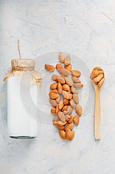 Almond milk in a bottle with a handful of seeds and a wooden spoon on a light background.