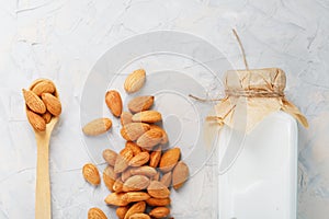 Almond milk in a bottle with a handful of seeds and a wooden spoon on a light background.