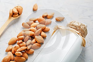 Almond milk in a bottle with a handful of seeds and a wooden spoon on a light background.