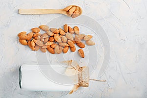 Almond milk in a bottle with a handful of seeds and a wooden spoon on a light background.