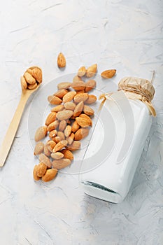 Almond milk in a bottle with a handful of seeds and a wooden spoon on a light background.