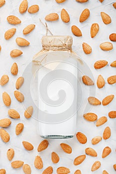 Almond milk in a bottle surrounded by a scattering of almond seeds on a light background