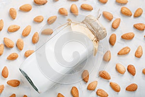 Almond milk in a bottle surrounded by a scattering of almond seeds on a light background