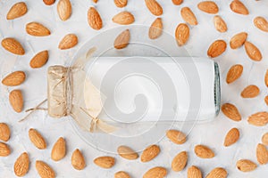 Almond milk in a bottle surrounded by a scattering of almond seeds on a light background