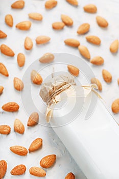 Almond milk in a bottle surrounded by a scattering of almond seeds on a light background