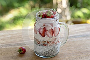 Almond milk chia pudding with fresh red strawberries, goji berries and oat flakes in a glass jar mug. Vegan raw breakfast. Chia