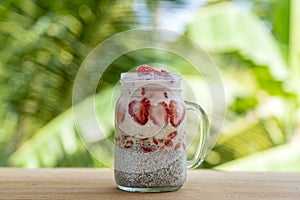 Almond milk chia pudding with fresh red strawberries, goji berries and oat flakes in a glass jar mug. Vegan raw breakfast. Chia