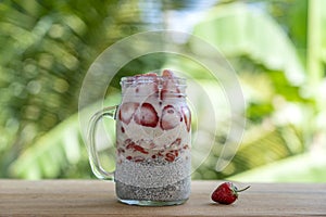 Almond milk chia pudding with fresh red strawberries, goji berries and oat flakes in a glass jar mug. Vegan raw breakfast. Chia