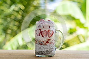 Almond milk chia pudding with fresh red strawberries, goji berries and oat flakes in a glass jar mug. Vegan raw breakfast. Chia