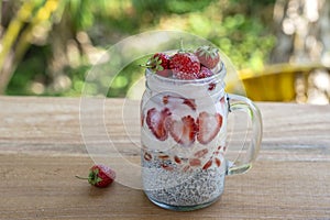 Almond milk chia pudding with fresh red strawberries, goji berries and oat flakes in a glass jar mug. Vegan raw breakfast. Chia