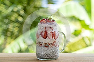 Almond milk chia pudding with fresh red strawberries, goji berries and oat flakes in a glass jar mug. Vegan raw breakfast. Chia