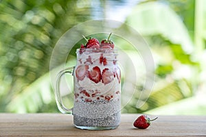 Almond milk chia pudding with fresh red strawberries, goji berries and oat flakes in a glass jar mug. Vegan raw breakfast. Chia