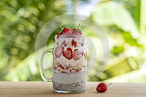 Almond milk chia pudding with fresh red strawberries, goji berries and oat flakes in a glass jar mug. Vegan raw breakfast. Chia