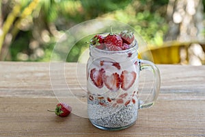 Almond milk chia pudding with fresh red strawberries, goji berries and oat flakes in a glass jar mug. Vegan raw breakfast. Chia